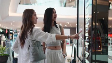 Bir alışveriş merkezinde interaktif dijital bir büfe hakkında bilgi arayan iki Asyalı arkadaş.