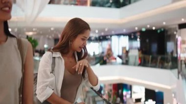 İki genç Asyalı kadın modern bir alışveriş merkezinin balkonundan bir mağazayı işaret ediyor.