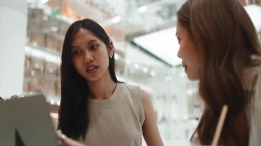 İki neşeli Asyalı kadın arkadaş bir tablet bilgisayar kullanırken oturup gülüyorlar.