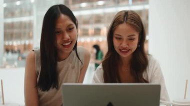 İki genç, gülümseyen bayan arkadaş laptopla çalışırken gülüp sohbet ediyorlar.