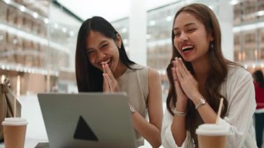 İki neşeli genç kadın, modern bir kahve dükkanında otururken dizüstü bilgisayarla video görüşmesi yapıyorlar.