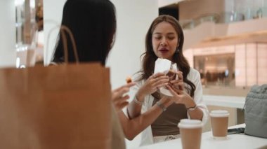 Modern bir alışveriş merkezindeki bir kafede yemek yiyip sohbet eden iki genç kadın.