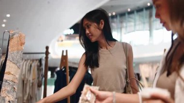 İki genç bayan arkadaş alışveriş merkezindeki bir butikte yeni kıyafetler seçiyorlar.