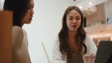 İki genç Asyalı kadın beyin fırtınası yaparken ve fikirleri paylaşırken hareketli bir konuşma yapıyorlar.