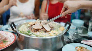 Geleneksel Moo Kra ta yemeğini paylaşan arkadaşlar, masada domuz ve sebze ızgara.