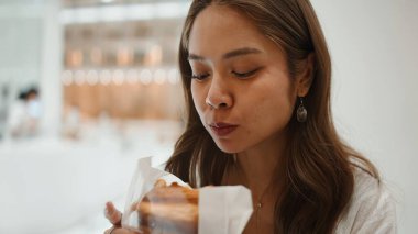 Parlak, modern bir kafede lezzetli bir kruvasan ya da hamur işi yiyen genç bir kadın gündelik bir anın tadını çıkarıyor.