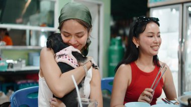 Taylandlı arkadaşlar moo krata yiyor, bir kadın sevimli köpeğine sevgiyle sarılıyor.