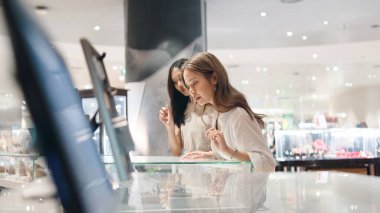 Genç Asyalı lezbiyen çift, parlak bir perakende mağazasında eşyalar karıştırıyor, gündelik anları paylaşıyor.