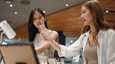 Perakende terapiden zevk alan iki Asyalı kadın, parlak bir dükkandan yeni ürünler seçiyorlar.