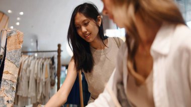 Genç Taylandlı kadınlar birlikte alışveriş yapıyor, çağdaş bir butikte kıyafet seçiyorlar.