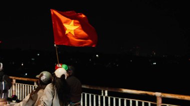 Vietnamlılar bir futbol zaferini kutluyorlar, ellerinde şehir ışıklarıyla ulusal bayrak sallıyorlar.