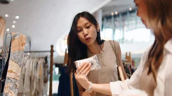 İki Taylandlı kadın alışveriş sırasında modern bir giyim mağazasında bir ürüne bakıyor.