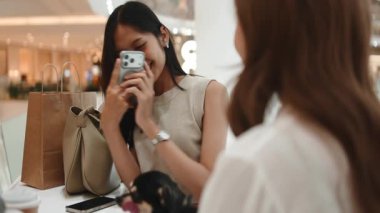 Güzel bir kadın alışveriş merkezinde bir arkadaşıyla otururken akıllı telefonuyla fotoğraf çekiyor.