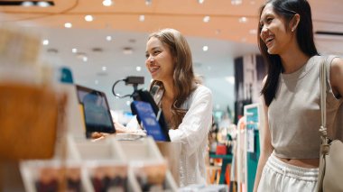 İki gülümseyen Asyalı genç kadın modern bir mağazada eğlenceli bir alışveriş gezisinin tadını çıkarıyor.