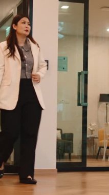 Kendine güvenen Asyalı iş kadını modern bir ofis binasında yürüyor ve merdivenlerden çıkıyor.