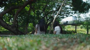 İki kız akıllı telefonlarına bakıyor ve şehir parkındaki çimlerin üzerinde çevrenin fotoğraflarını çekiyor.