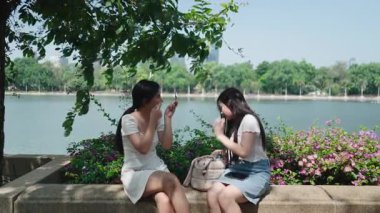 İki genç kadın gölün kenarında oturmuş makyaj yapıyor ve şehir parkının tadını çıkarıyorlar.