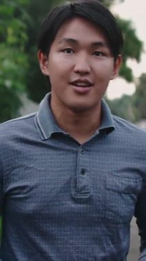 Yakışıklı Taylandlı bir adam doğal bir parkta buluşurken sakin bir ifadeyle yürüyor ve konuşuyor.