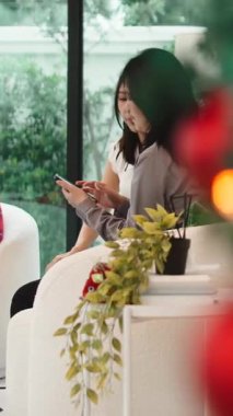 Arkadaşça bir toplantı sırasında koltukta oturan ve cep telefonunda gezinen iki genç kadın.