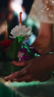 Geleneksel Tayland kutlamaları sırasında ellerinde mumla dekoratif bir Krathong 'u suya koyan eller.