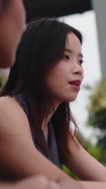 Genç Asyalı bir kadın açık hava kafeteryasında bir arkadaşıyla keyifli bir sohbet ediyor.