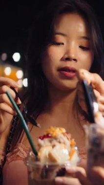 Geceleri arkadaşlarıyla dışarıda dondurma yiyen gülümseyen Asyalı genç bir kadının fotoğrafını çek.