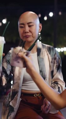 Kemoterapi yüzünden saçı dökülen Asyalı kadın dışarıda eğleniyor ve arkadaşlarıyla gülüyor.