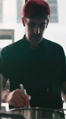 Modern bir restoranın mutfağında, çelik tencerede yemek karıştıran genç profesyonel şef.