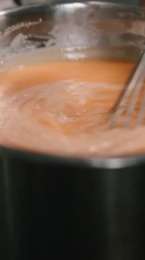 Profesyonel şef, paslanmaz çelik bir tencerede güçlü bir şekilde çırpınan kremalı portakal sosu hazırlıyor.