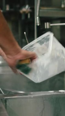 Mutfak işçileri kirli plastik bir kabı metal bir lavaboda süngerle yıkıyorlar.