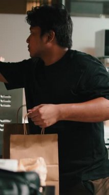 Genç bir erkek işçi servis için restoranın mutfağında bir kese kağıdına yemek dolduruyor.