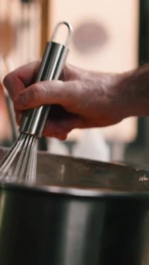 Erkek aşçı el kremalı bir sıvıyla profesyonel bir mutfak ortamında metal çırpıcıyı karıştırıyor.