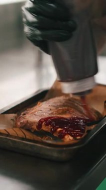 Siyah eldivenli profesyonel şef bol barbekü soslu domuz pirzolası pişiriyor.