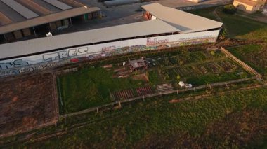 Şehrin eteklerinde grafiti olan bir sanayi deposunun yanındaki kamu bahçesinin havadan görüntüsü - 4K Yatay