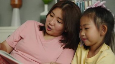 Asyalı anne ve kız birlikte iyi vakit geçiriyorlar, oturma odasında kitap okuyorlar.