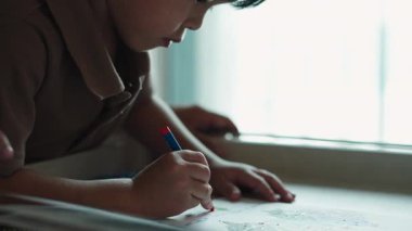 Genç yaratıcı çocuk pencerenin yanında pastel boyalarla kağıda çizim yaparken konsantre oluyor.