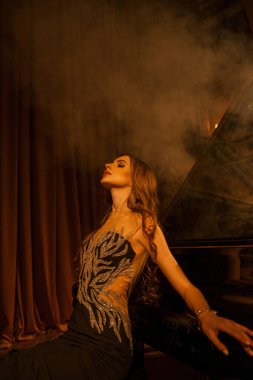 Tiyatroda kuyruklu piyanonun yanında poz veren güzel genç bir kadın.