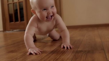Bebek bezi takmış, gülen şirin bir bebek. Evdeki neşeli çocuğun ahşap zemininde sevinçle sürünüyor.