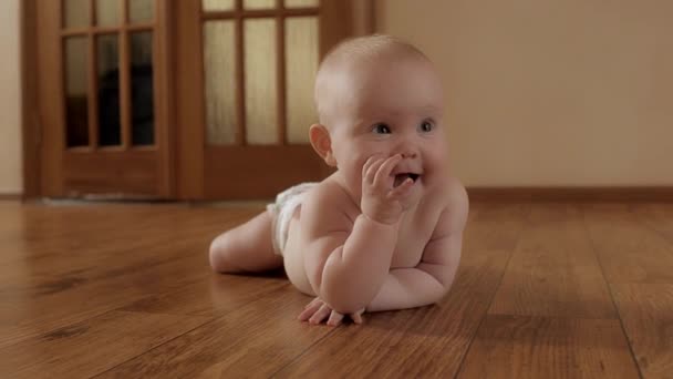 Забавна маленька дитина в памперсі лежить на дерев'яній підлозі облизуючи пальці розслабляючись насолоджуючись щасливим дитинством — стокове відео