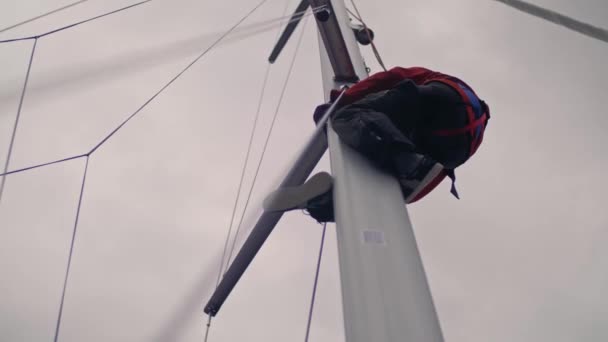 Actieve man klimmen op mast van sport jacht zet grootzeil zee regatta lage hoek bij bewolkte donkere lucht — Stockvideo