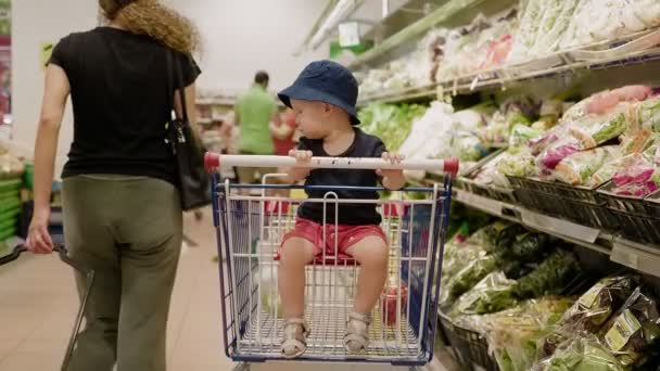 坐在购物车里戴着一顶夏帽的可爱的小男孩 — 图库视频影像