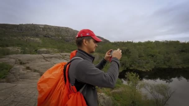 Mochilero masculino fotografiando el uso natural del lago smartphone en la superficie del agua del estanque de roca de montaña — Vídeos de Stock
