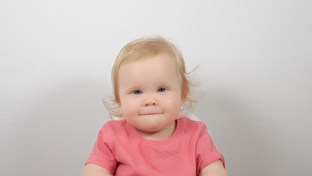笑顔小さな赤ちゃん身に着けていますピンクジャンパーで座っています給餌椅子posing絶縁上の白い背景 — ストック動画