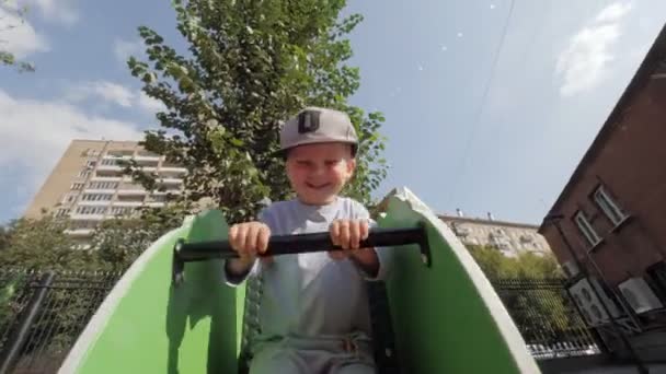 Adorable little boy laughing swinging on swing at child playground cheerful male kid walking outdoor — Stock Video