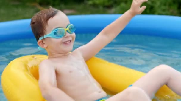 Menino feliz em óculos de proteção flutuando na bóia de segurança na piscina de borracha inflável — Vídeo de Stock