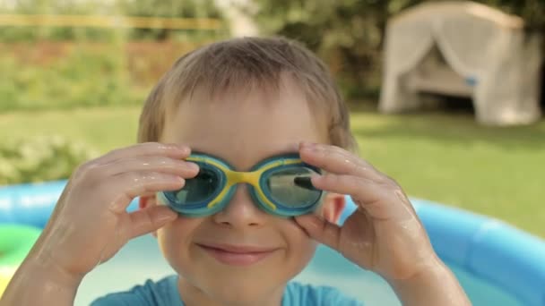 Closeup face of little boy taking off goggles relaxing outdoor near inflatable rubber swimming pool — стоковое видео