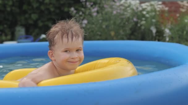 Engraçado menino tomando banho de sol relaxante deitado na boia salva-vidas amarela na piscina de borracha inflável — Vídeo de Stock