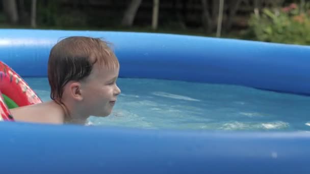 Divertente bambino ragazzo galleggiante in sicurezza boa anguria circondato da spruzzi d'acqua vista laterale — Video Stock