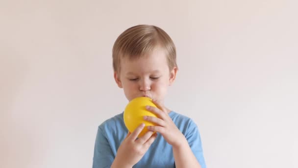 Fröhlicher kleiner Junge bläst gelben Luftballon feiert Urlaub mit Spaß posiert isoliert — Stockvideo