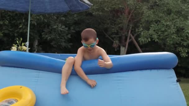 Menino alegre escalada jogando relaxante na piscina de borracha inflável com guarda-chuva — Vídeo de Stock
